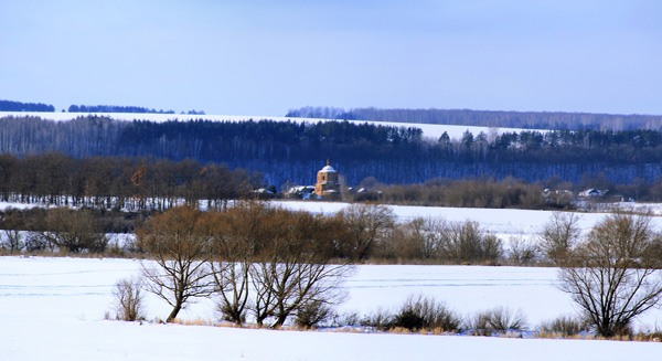 Красивый зимний пейзаж: солнце, снег, перелески и заброшенная церковь вдали за рекой.